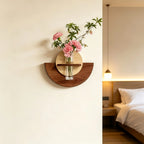 A wall-mounted wooden shelf and vase holder with pink flowers, shown mounted on an off-white wall in a softly lit bedroom setting.