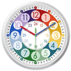 A colorful children's educational wall clock with a white outer ring, a white center, and colored hour sections from blue to green to yellow to red. The clock has multiple hands in different colors and numbers 0 through 24 around the dial.
