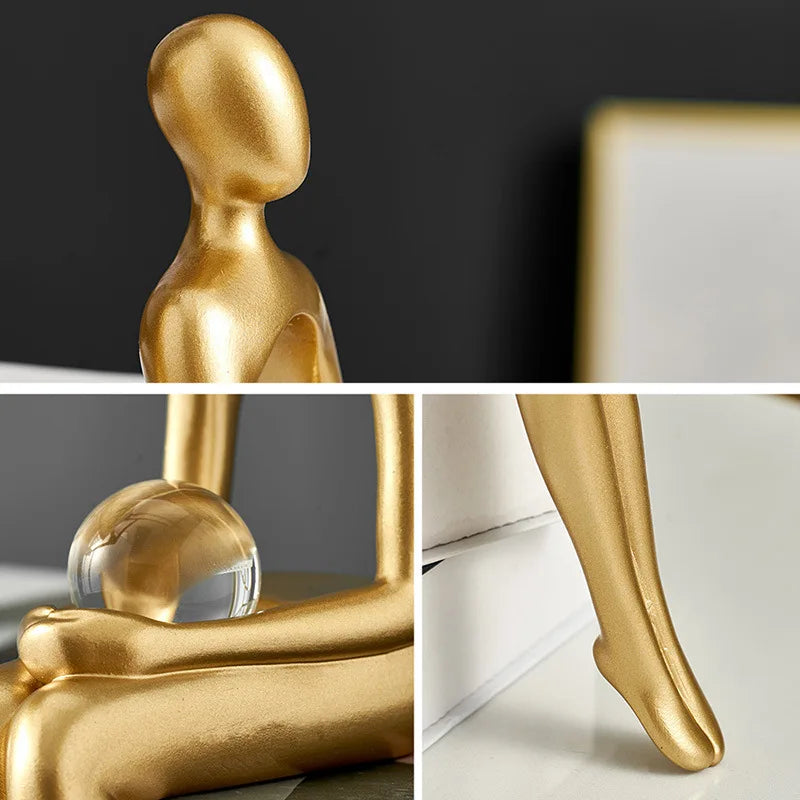 Golden abstract sitting figurine holding a clear glass orb, close-up details of its textured surface, leg, and hands.