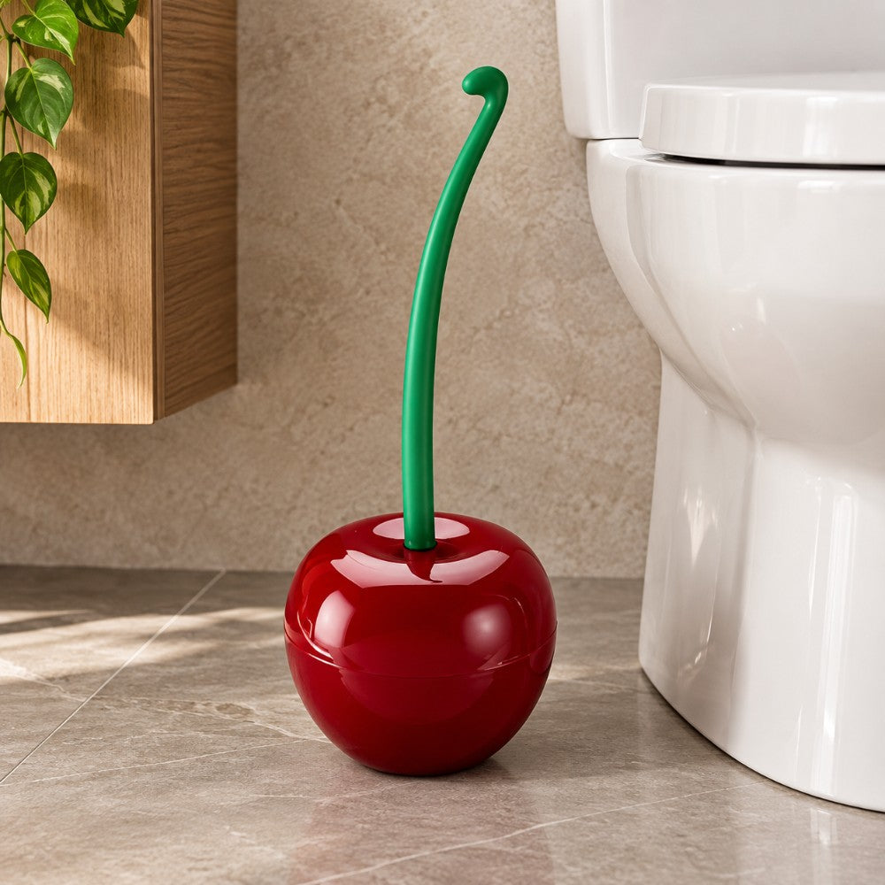 Glossy red holder shaped like a cherry with a green stem handle, sitting on a tiled floor next to a white toilet.