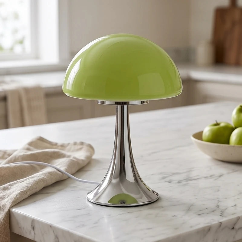 A green mushroom-shaped glass lamp with a shiny chrome base sits on a white marble kitchen counter.
