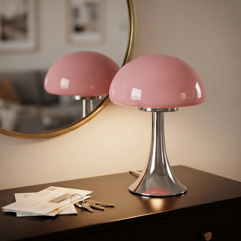 Pink mushroom-shaped table lamp with a shiny silver base on a dark wooden table next to a brass-framed mirror.