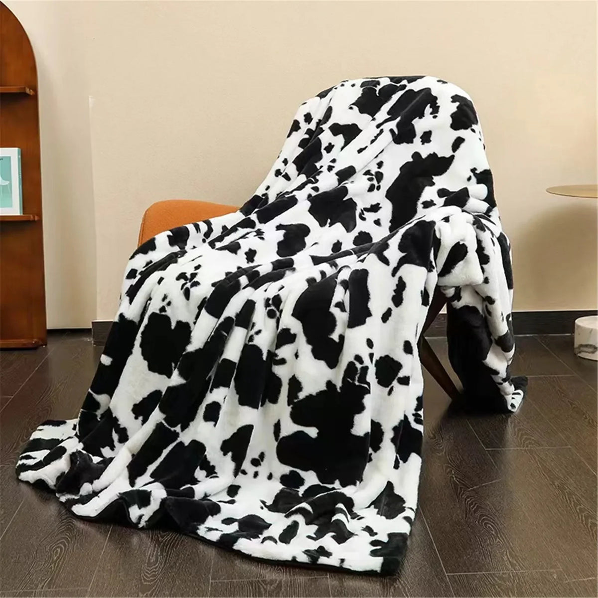 Soft black and white cow print plush blanket draped over a brown armchair, pooling onto a dark wooden floor.