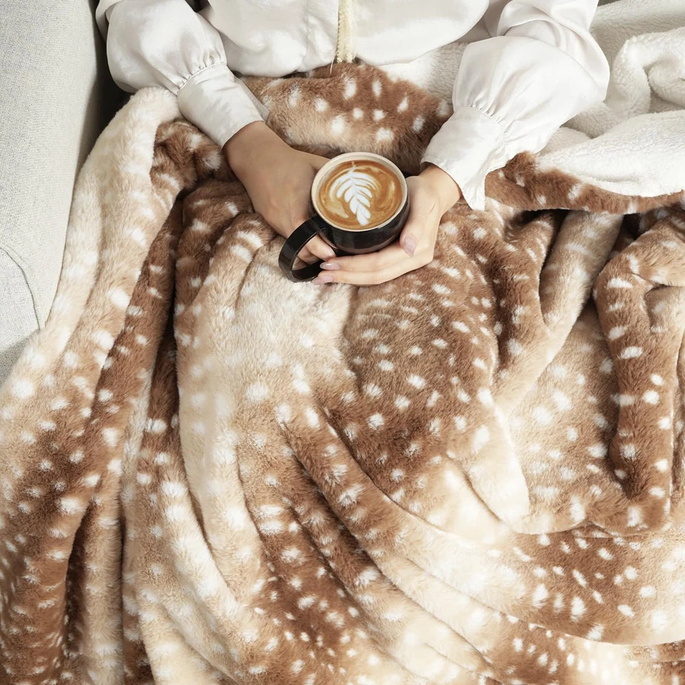 Woman holding a black mug with latte art, cozy under a plush brown and white spotted throw blanket.