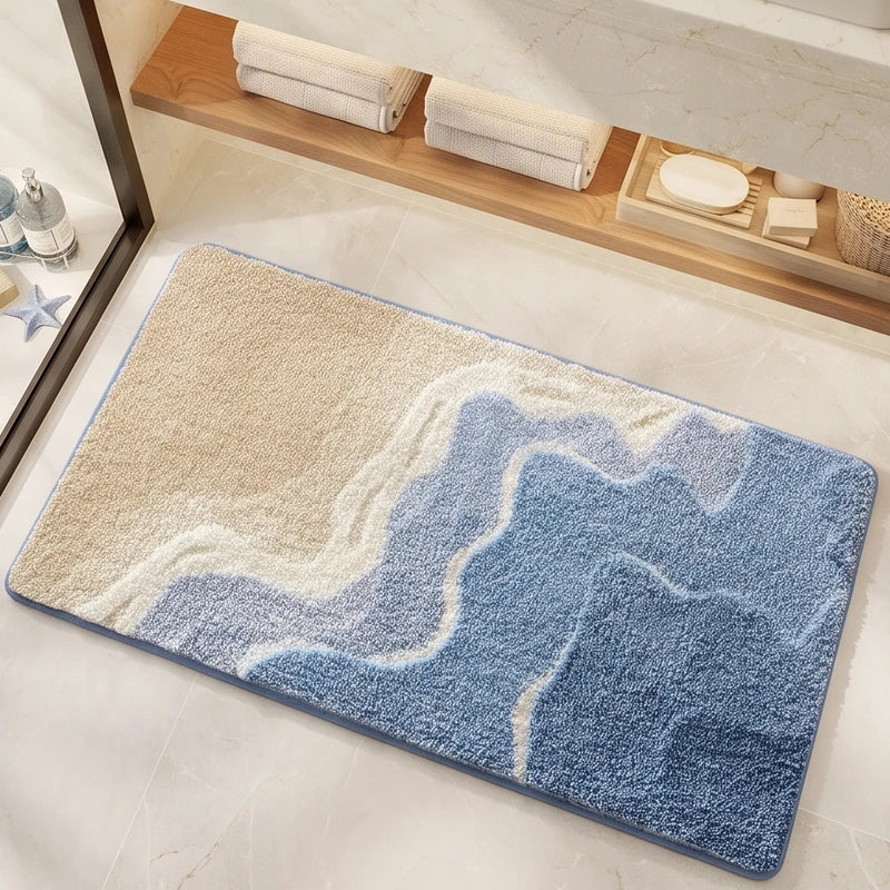 A rectangular rug with a plush texture displays a wave-like pattern in shades of sandy beige, light blue, and deep blue.