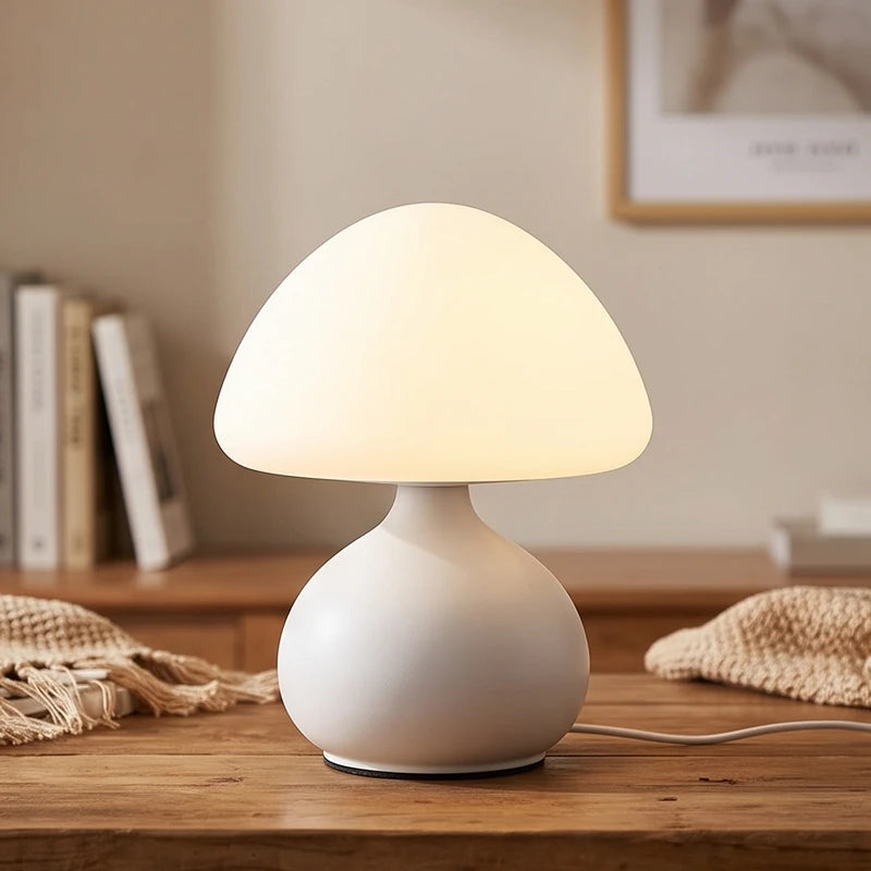 White mushroom-shaped table lamp with an illuminated frosted glass dome on a wooden desk with books.