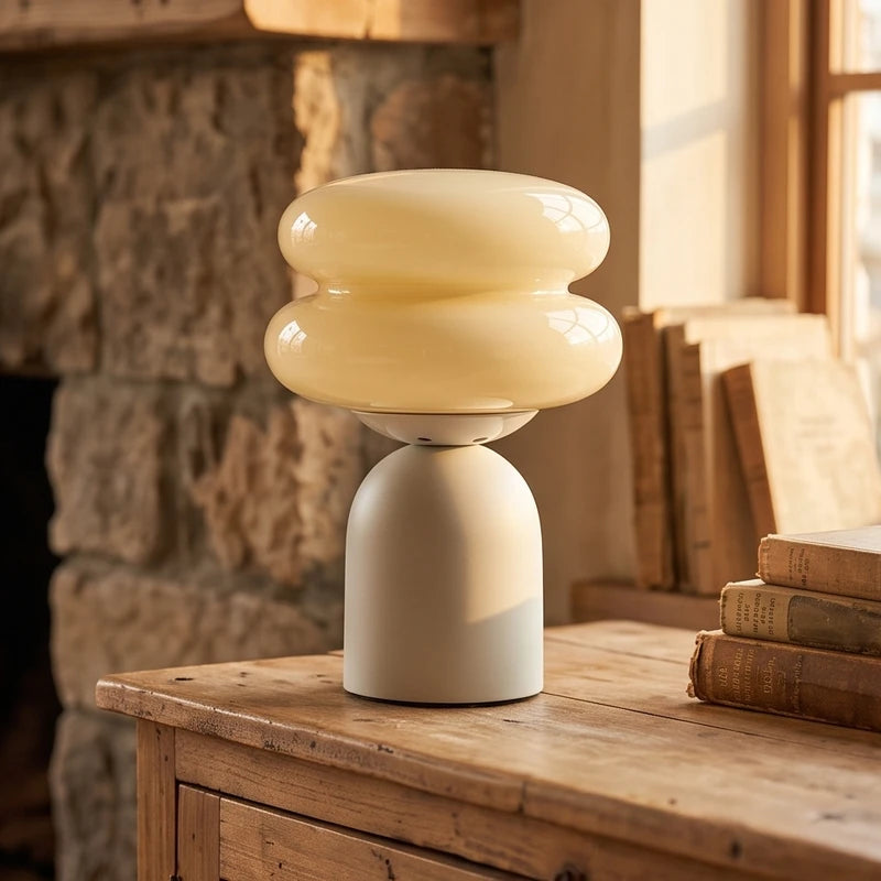 Creamy hourglass glass shade on a rounded beige base, placed on a wooden table with books.