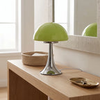 Bright lime green mushroom lamp with a shiny chrome base sits on a light wood console table beside a mirror.
